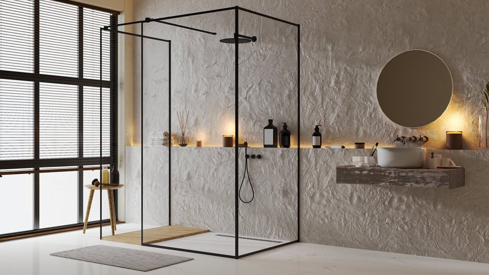 A modern bathroom with a minimalist design featuring a glass shower enclosure, a round mirror above a floating sink, soft lighting, and various toiletries on the shelf. A wooden stool and a large window complete the space's aesthetic.