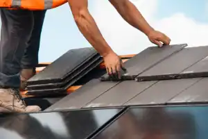 A worker in boots and safety vest installs dark roof tiles for a General Contractor in Suffolk County, NY.