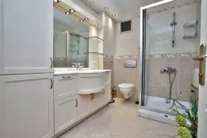 Modern bathroom in NY featuring white cabinets, large mirror, sink, wall-mounted toilet, glass shower enclosure, and beige tiled walls and floor. Upgrade your space with a trusted general contractor Suffolk County recommends.